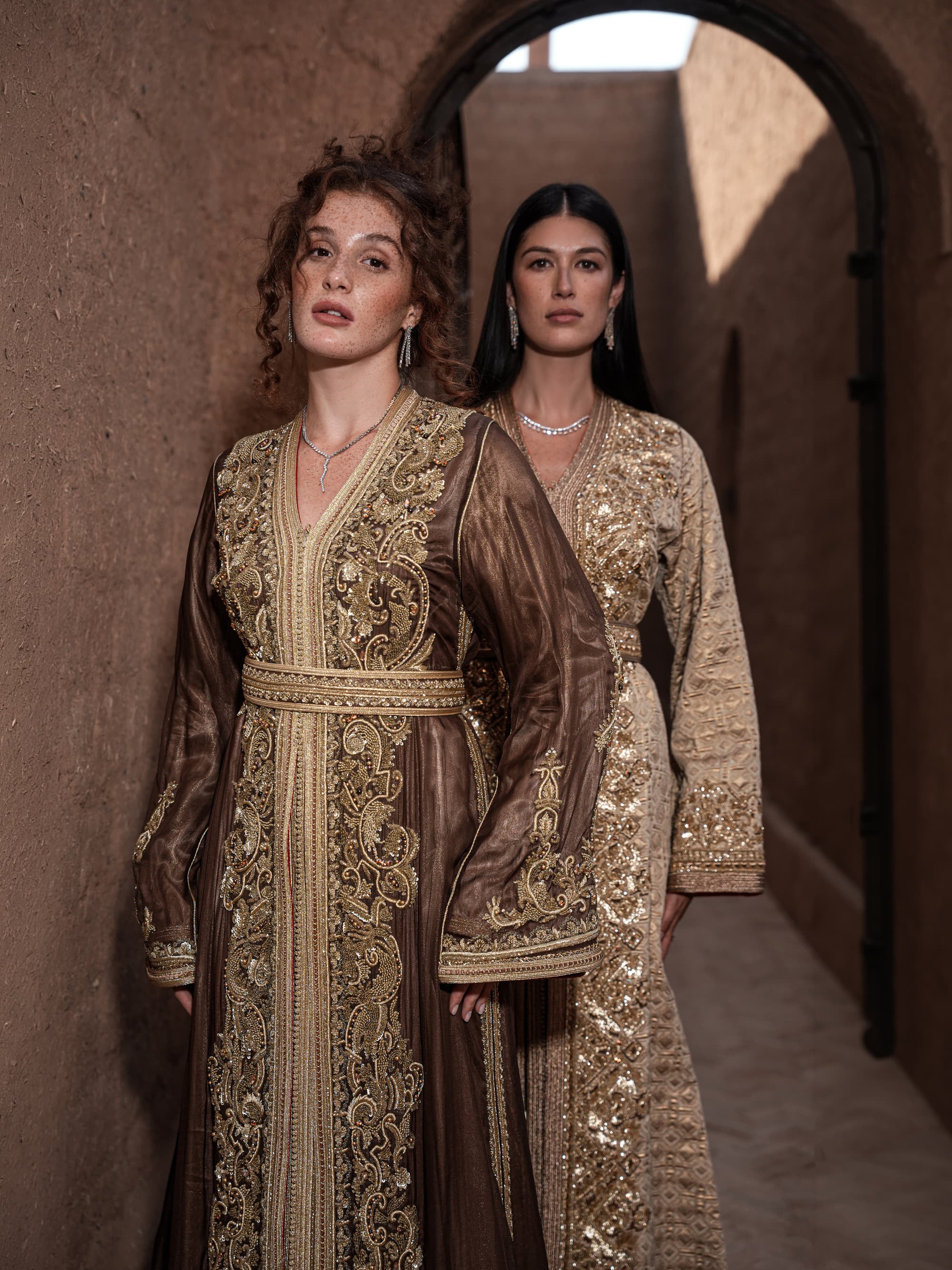 Bronze Reverie lamé organza Moroccan kaftan with gold embroidery, worn open over a champagne dress, shown alongside a second look