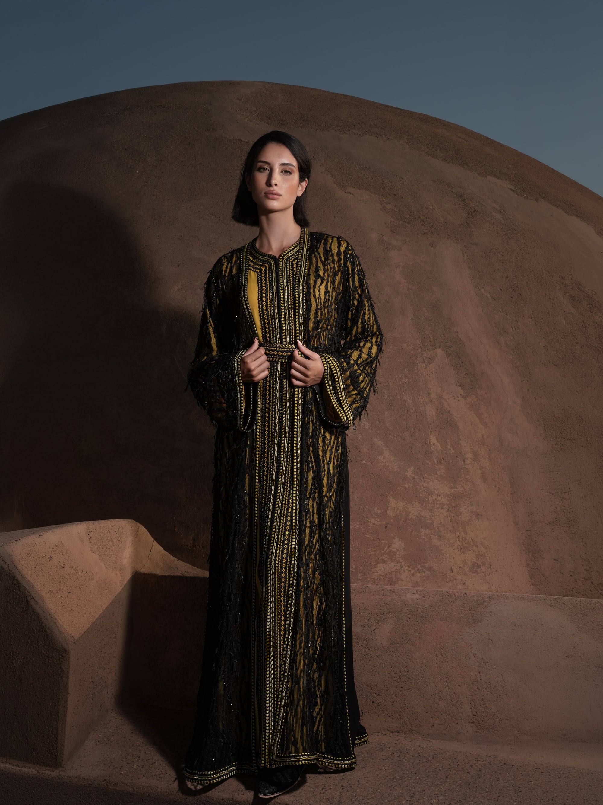 Onyx Serenade fringed black lace Moroccan kaftan over a mustard-gold dress, full-length view