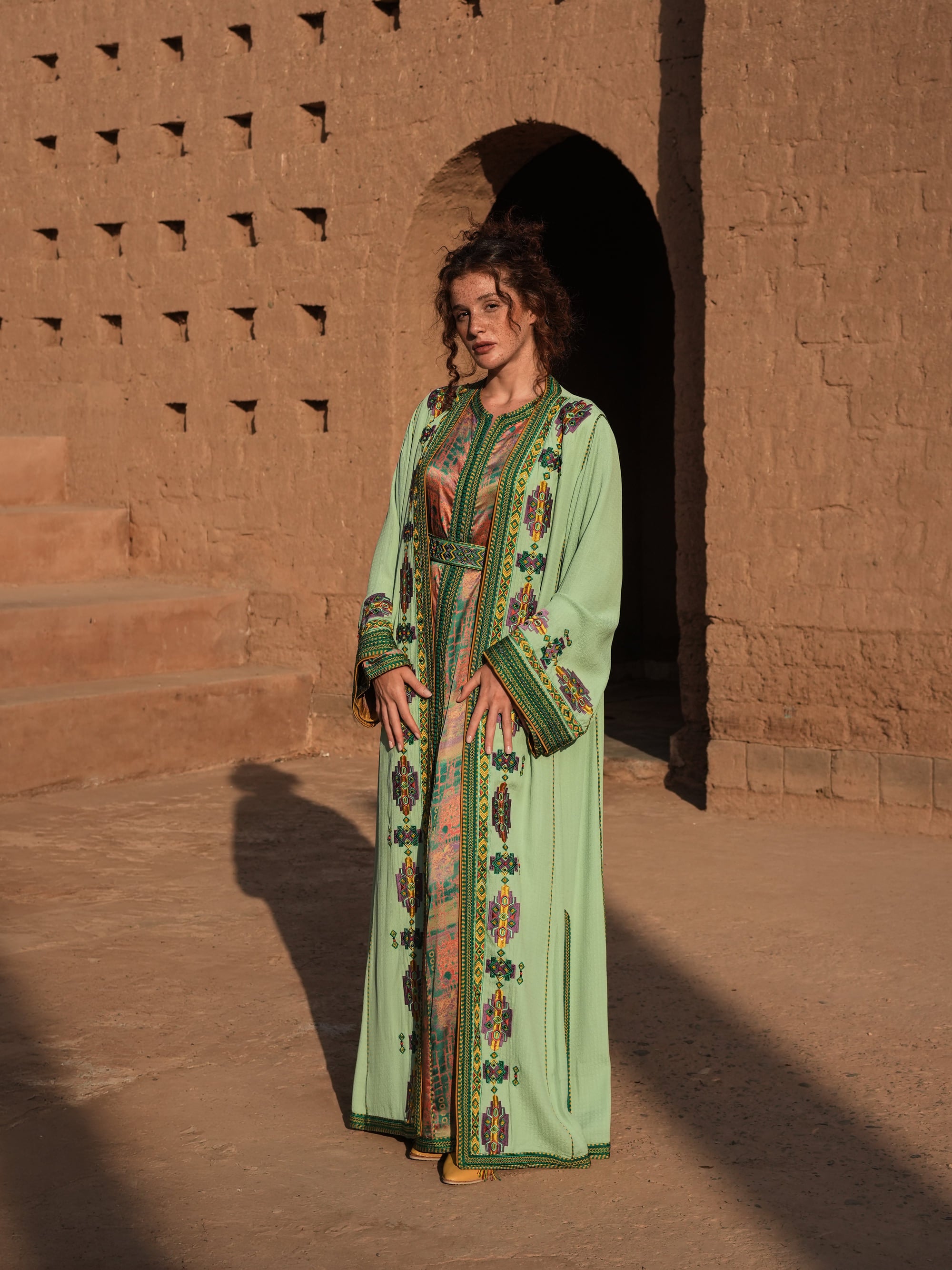 Anise Pavilion anise green Moroccan kaftan with Berber braid trims over a printed dress, full-length view
