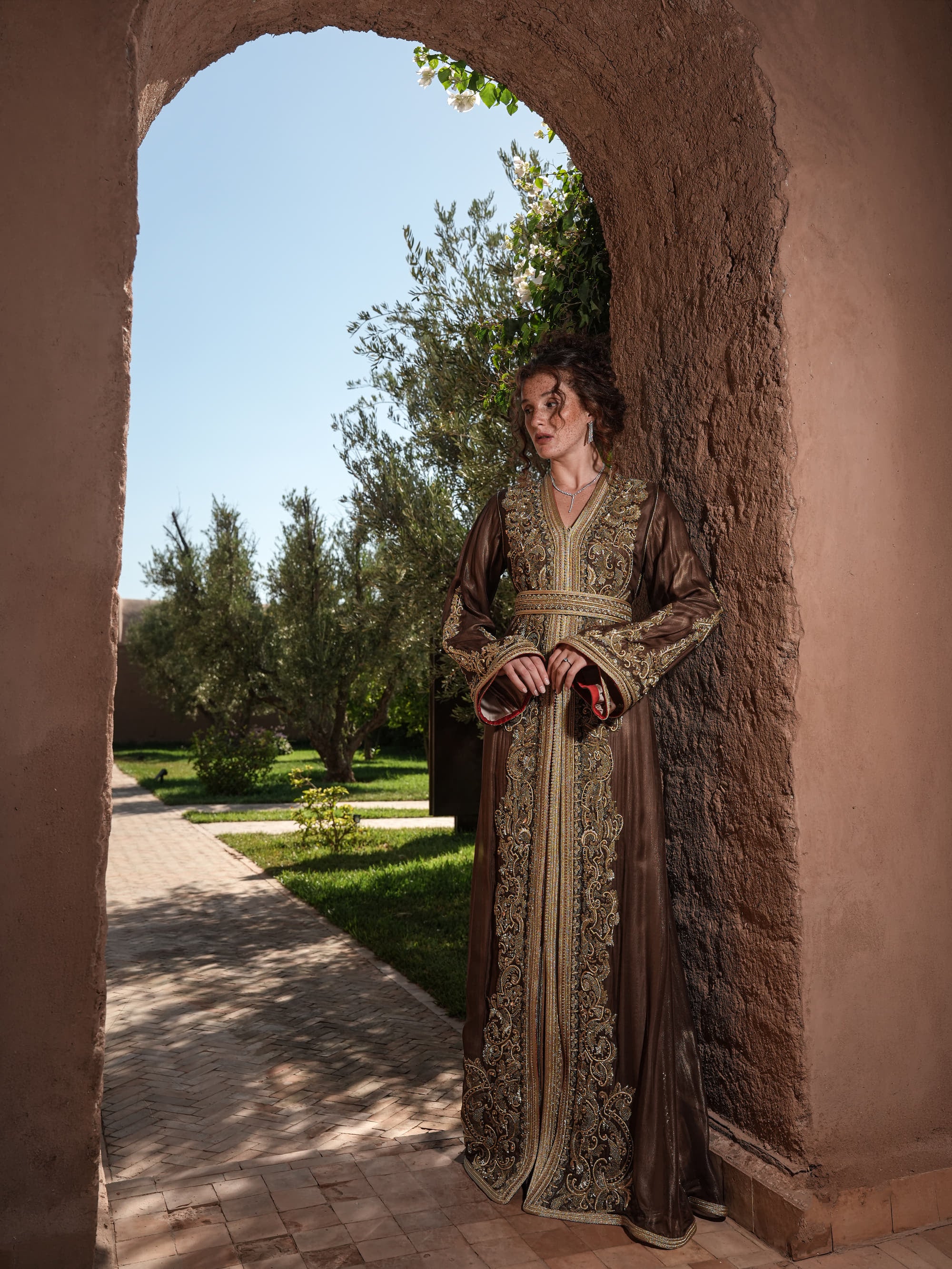 Bronze Reverie lamé organza Moroccan kaftan with gold embroidery, worn open over a champagne dress, full-length view