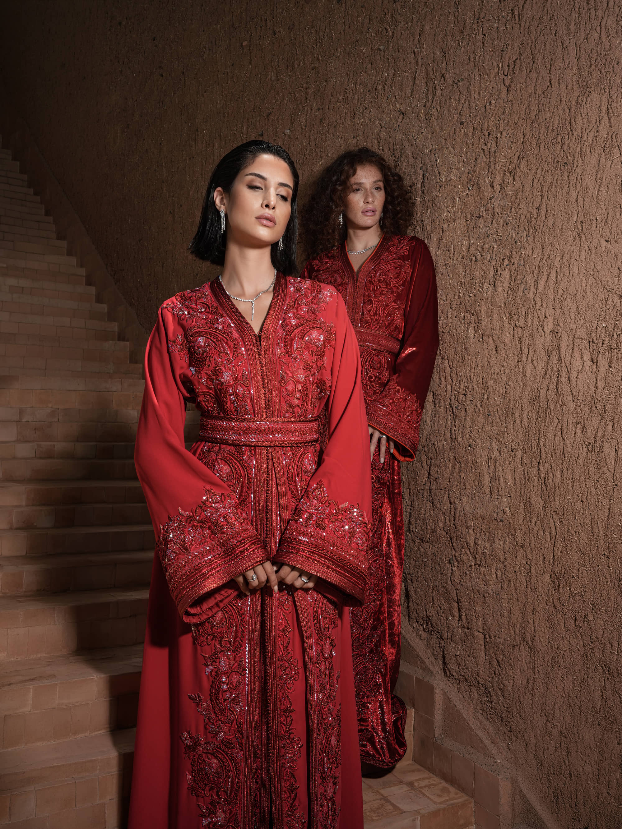 Carmine Cadence red crepe Moroccan kaftan with sequined paisley embroidery, braided belt and flared sleeves, shown alongside a second look