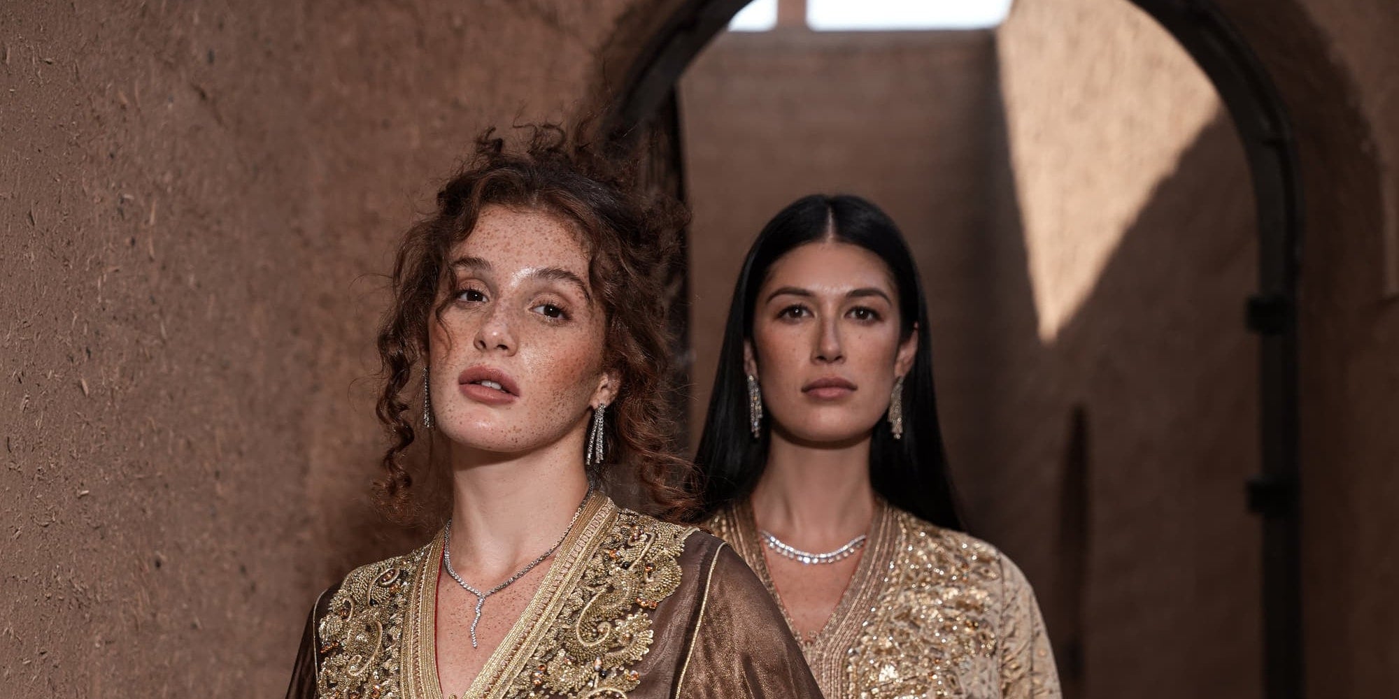 Two Moroccan kaftans in bronze and gold with dense gold embroidery, worn under a Marrakech archway