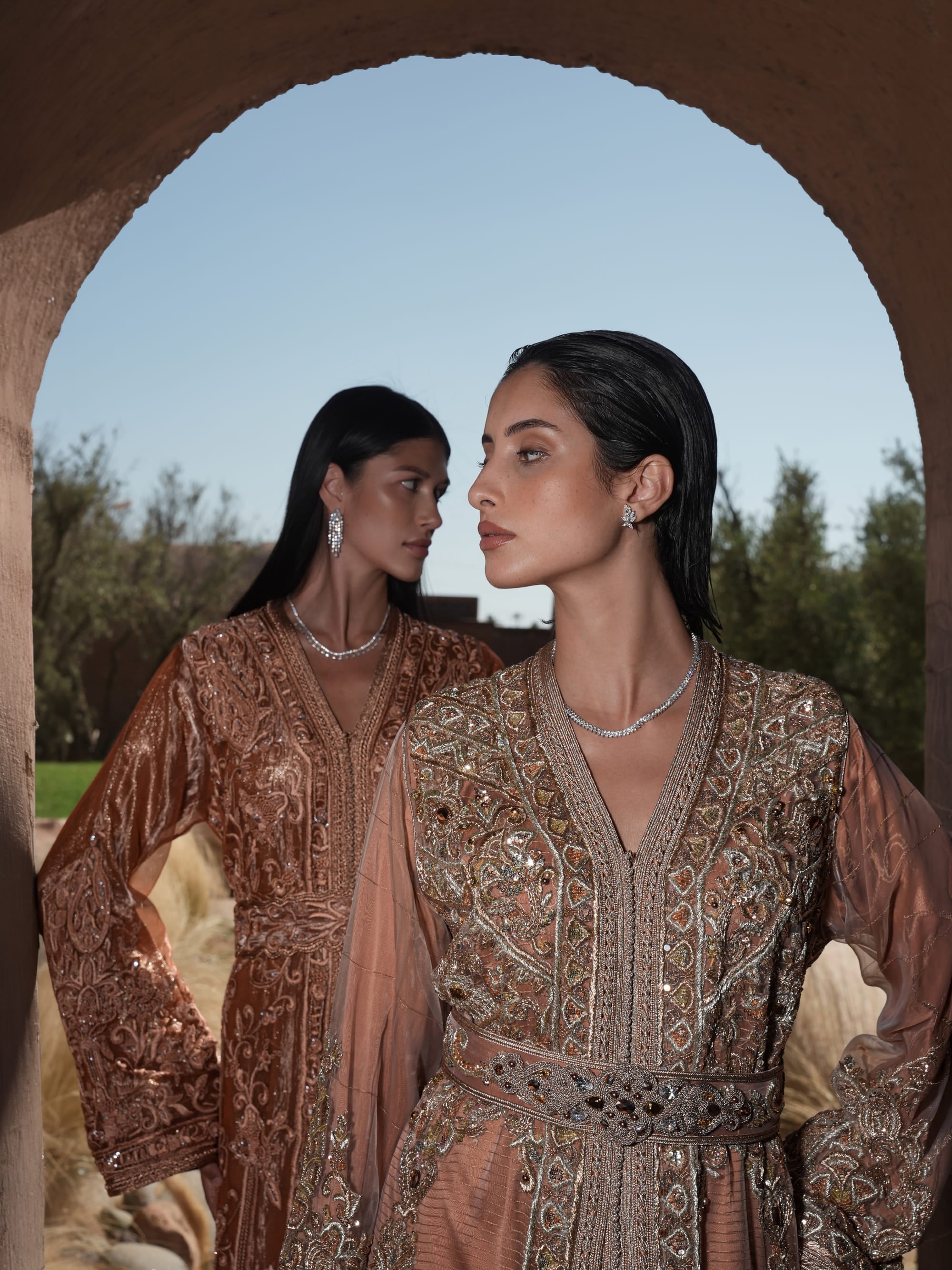 Rosewood Aurora copper-rose organza Moroccan kaftan with silver embroidery and jewelled belt, shown alongside a second look